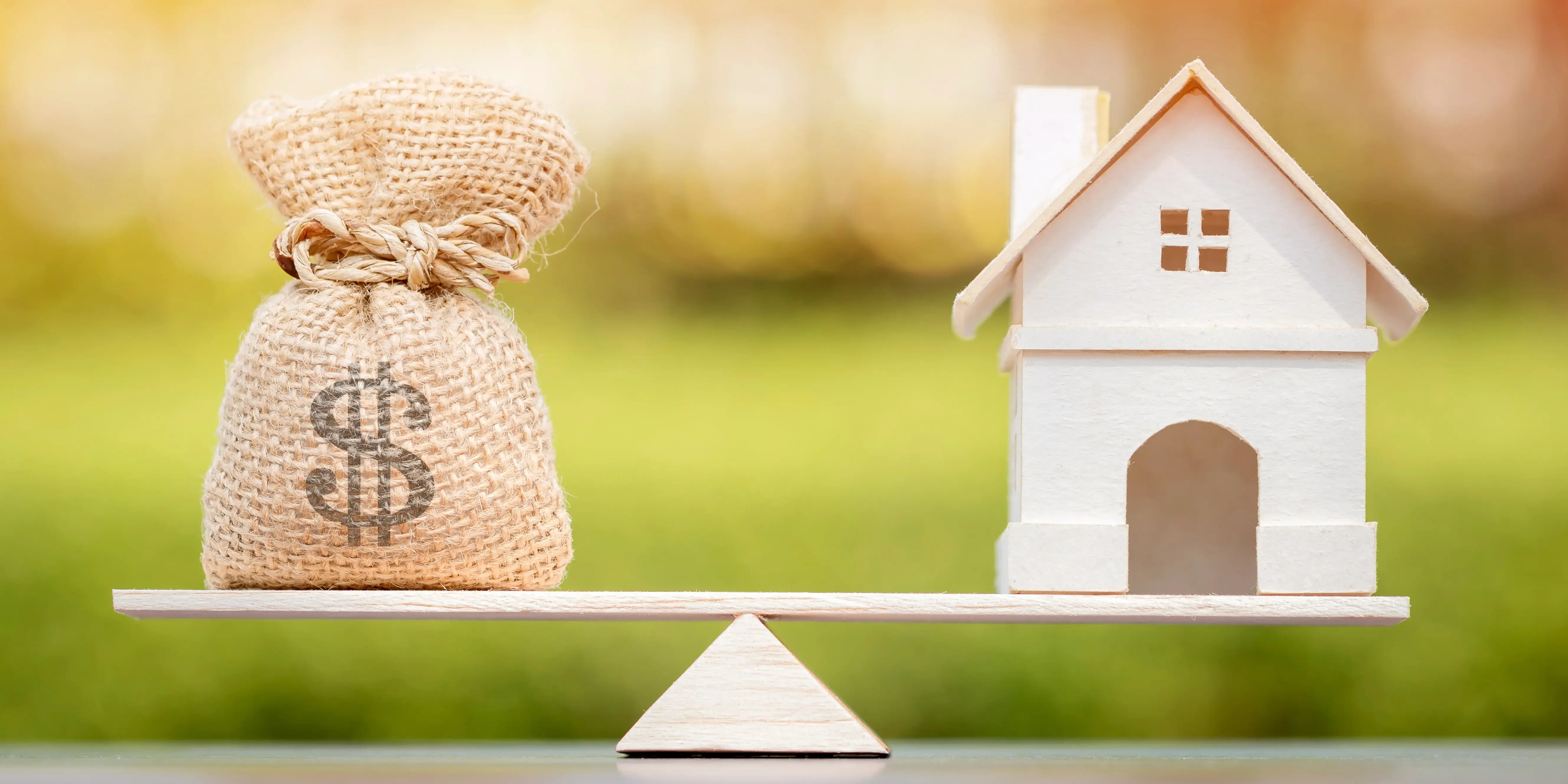 Balanza con un costal de dinero del lado izquierdo y una casa de madera del lado derecho haciendo referencia a comprar casa casi sin dinero