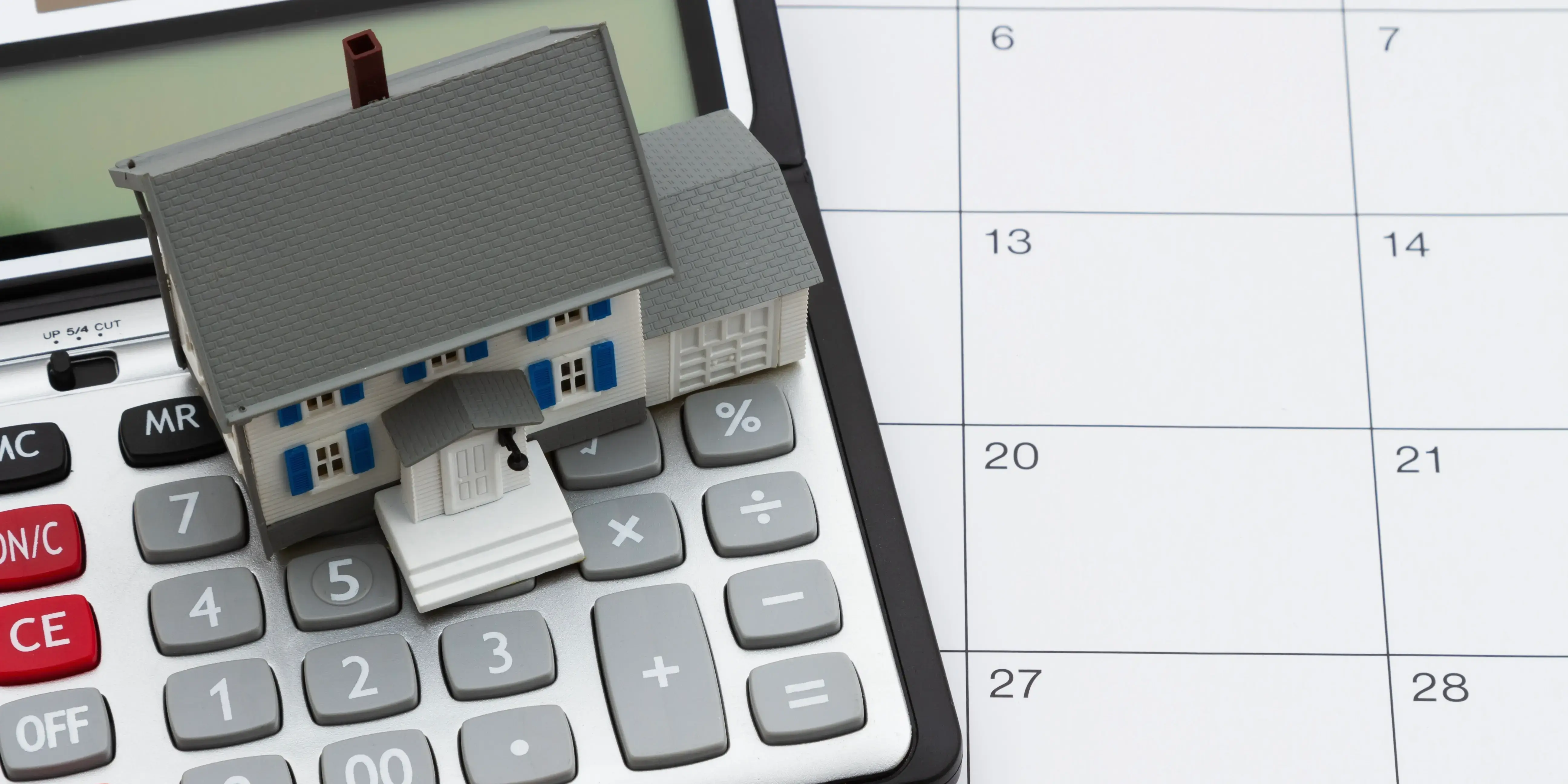 Casa de madera y una calculadora sobre un calendario donde se anotan las mensualidades que se tienen que pagar del crédito conyugal FOVISSSTE