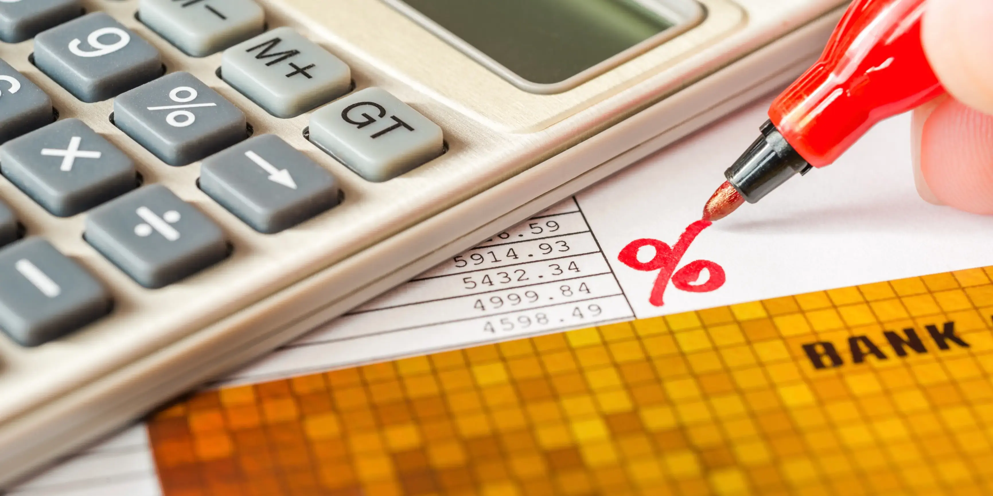 Hoja con el cálculo de los intereses pagados por anticipado de un préstamo, una calculadora y una tarjeta de crédito sobre la mesa