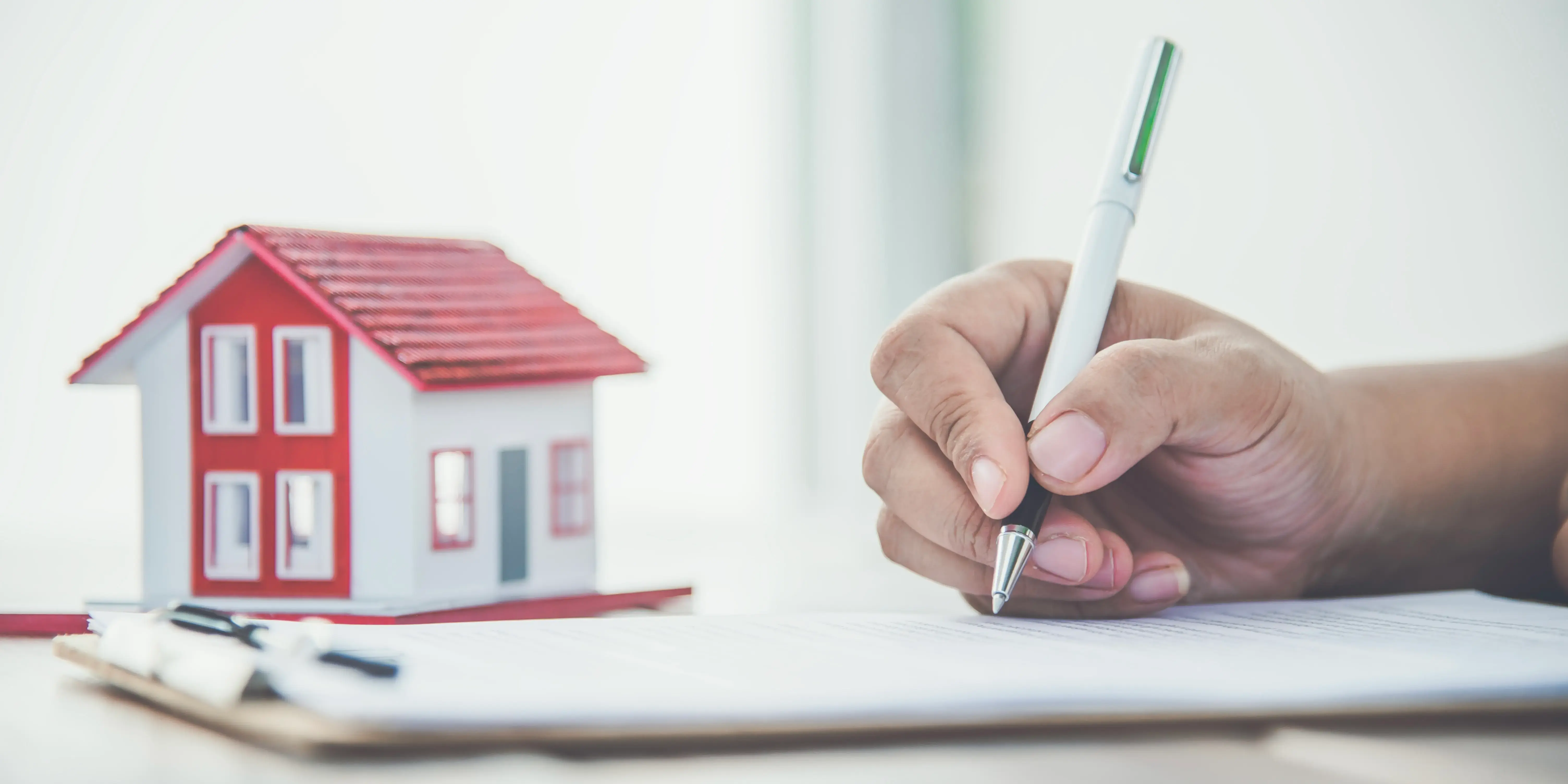 Hombre firmando unos papeles de su crédito Infonavit y al fondo se ve una casa de madera