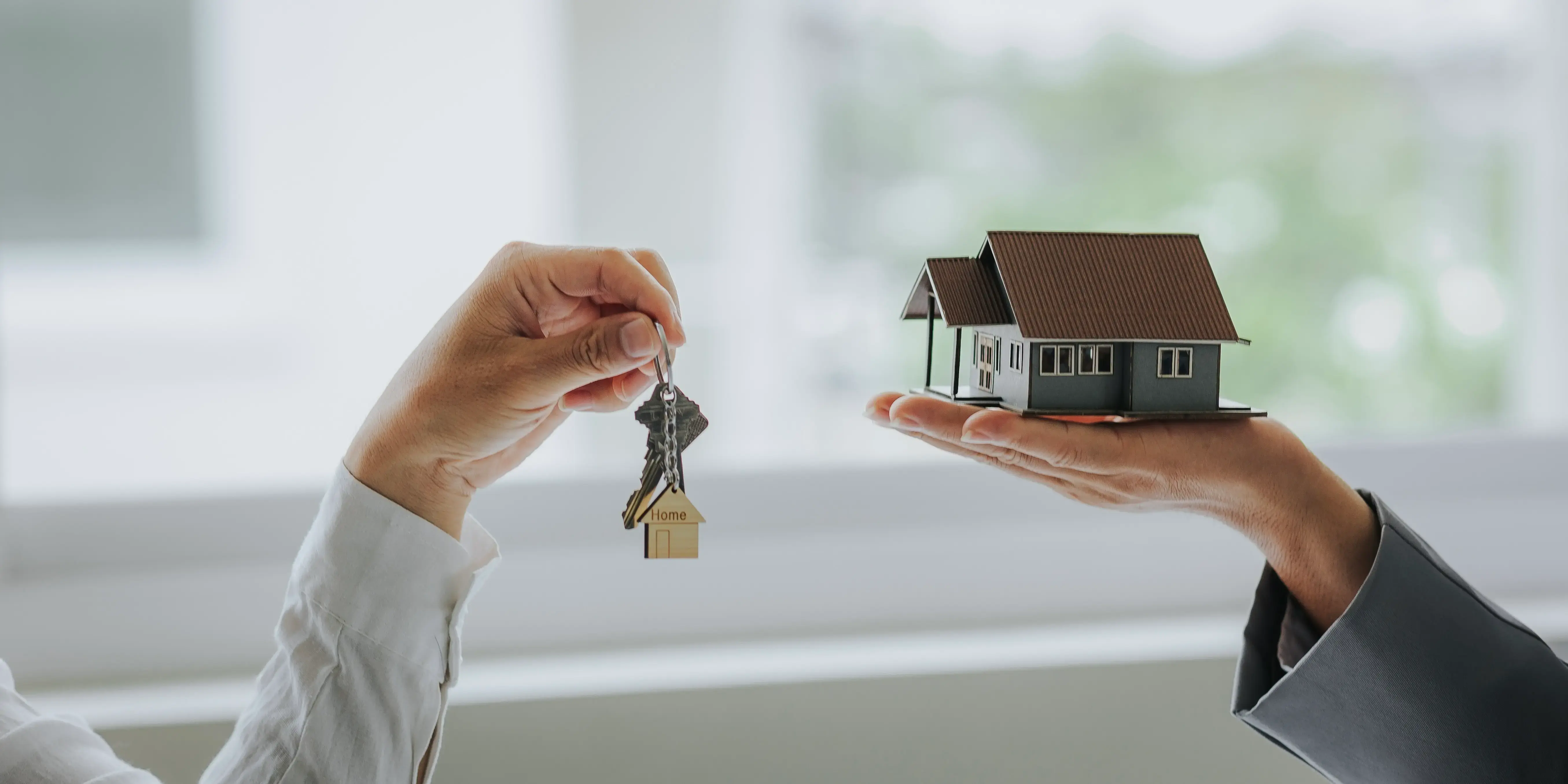 Manos de asesores inmobiliarios sosteniendo unas llaves y una casa respectivamente para comprar casa sin Infonavit