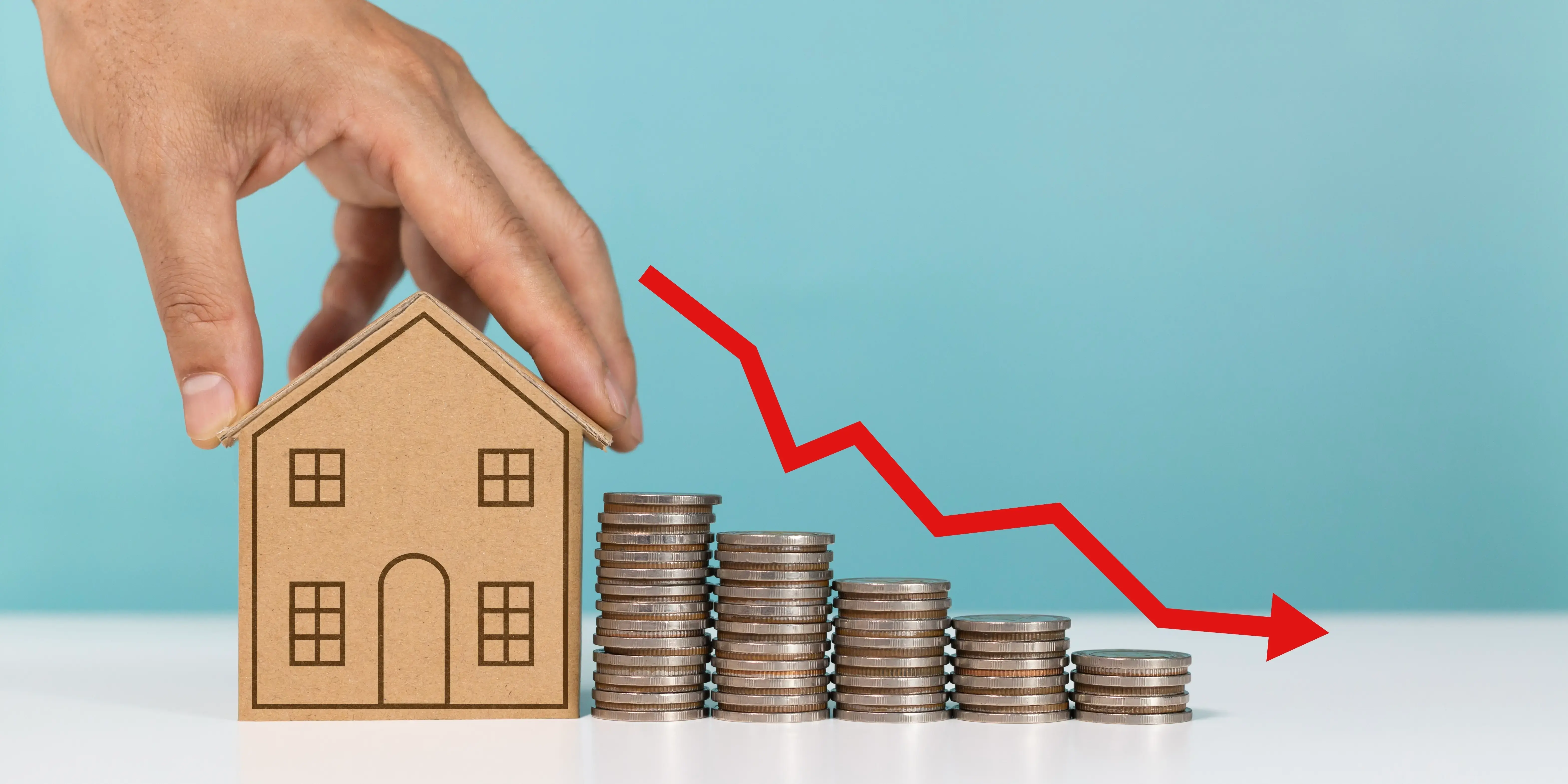 Mini casa modelo con pila de monedas y flecha hacia abajo de Indicando crédito hipotecario para vivienda accesible