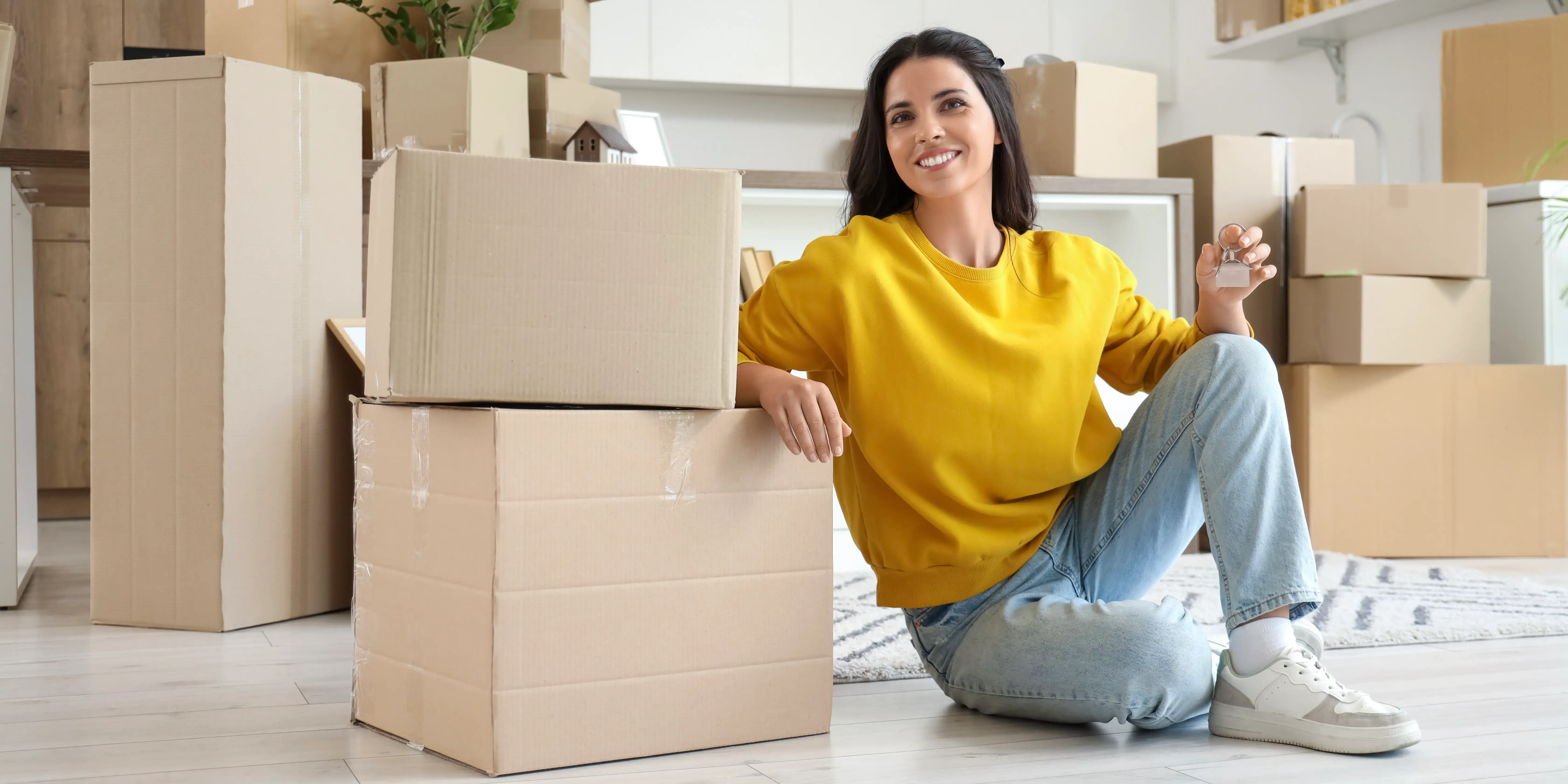 Mujer sosteniendounas llaves y rodeada de cajas de mudanza, el último paso para comprar una casa