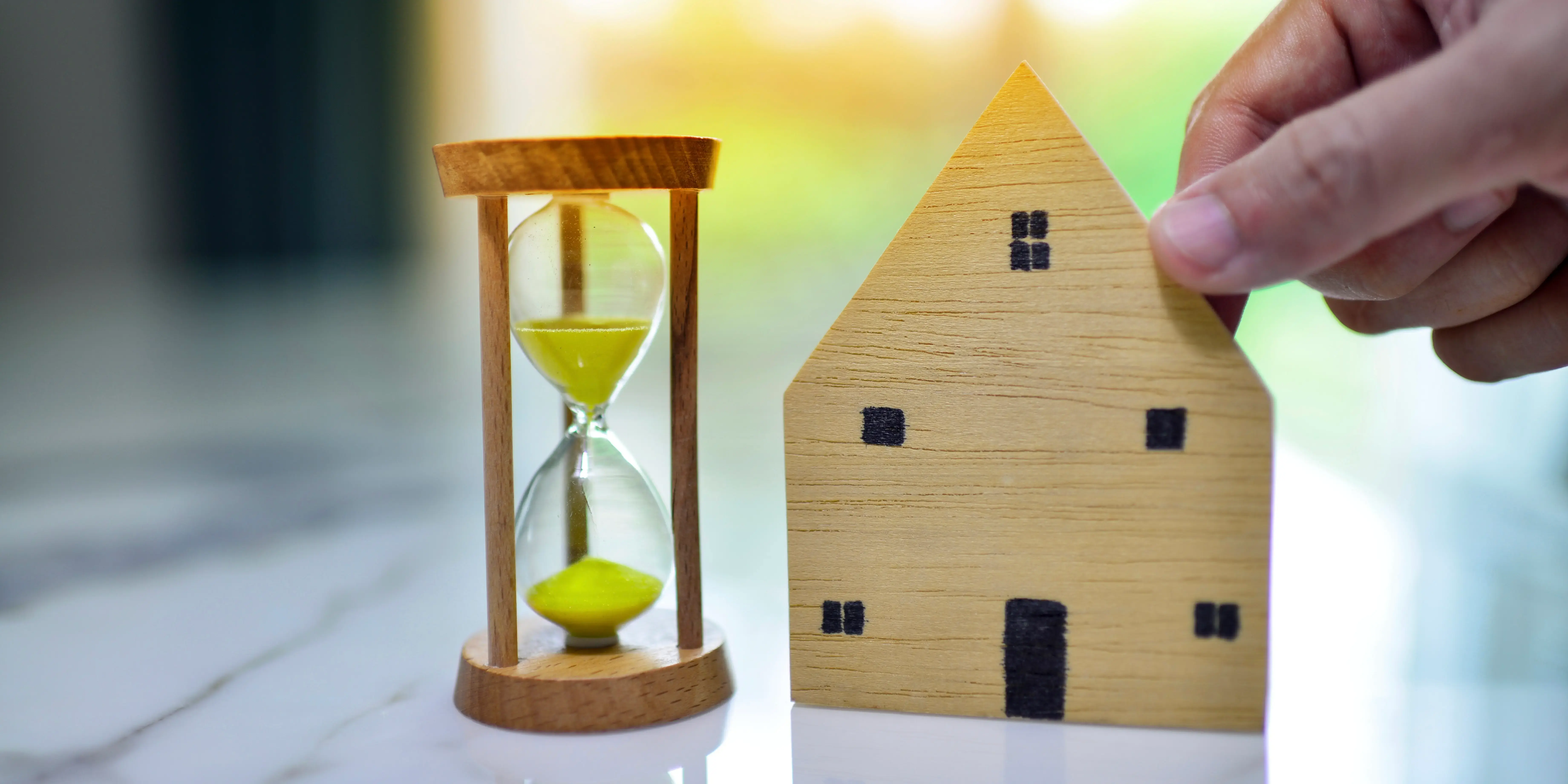Persona agarrando un mini modelo de casa de madera con un reloj de arena a un lado, eligiendo liquidar la hipoteca antes de tiempo 