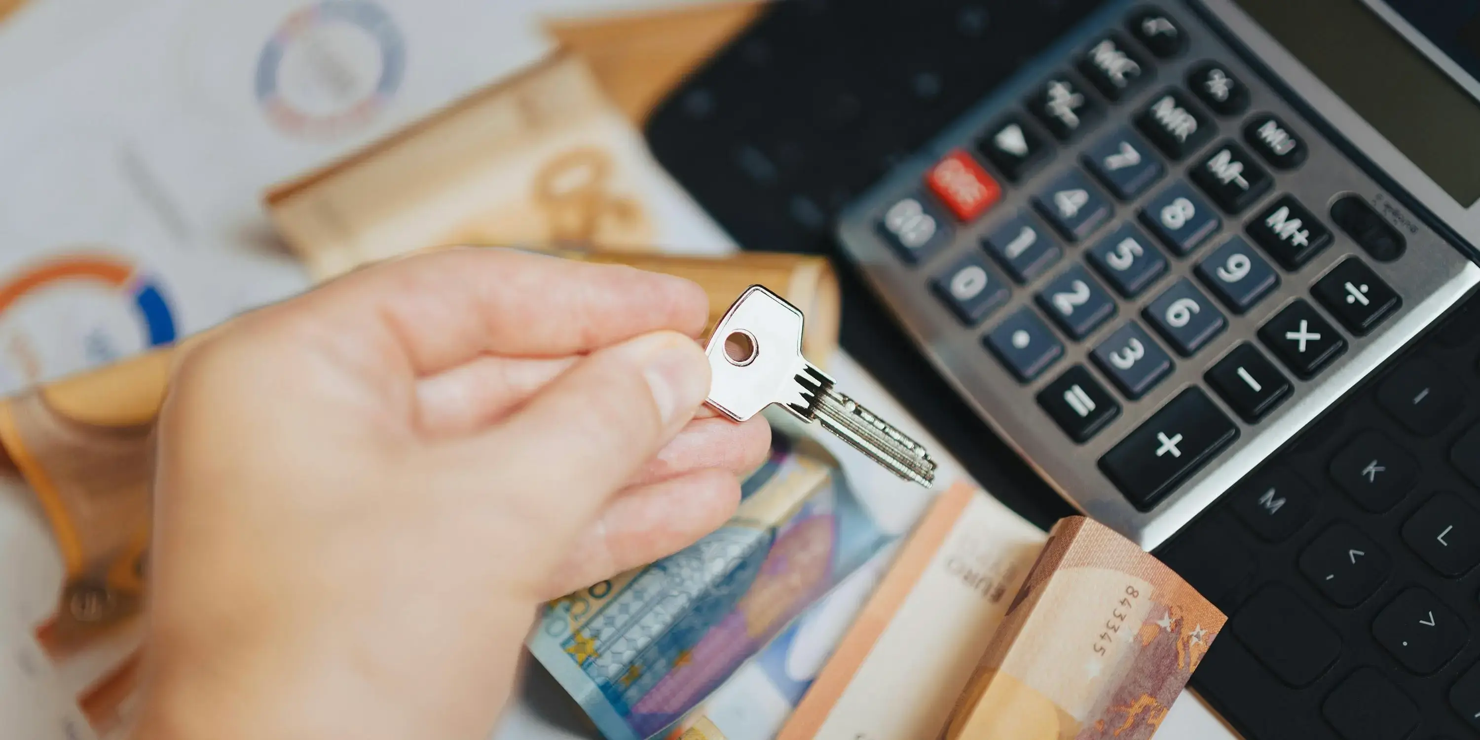 Mano sosteniendo llave con calculadora y billetes al fondo. Hipoteca 15 vs 30 años