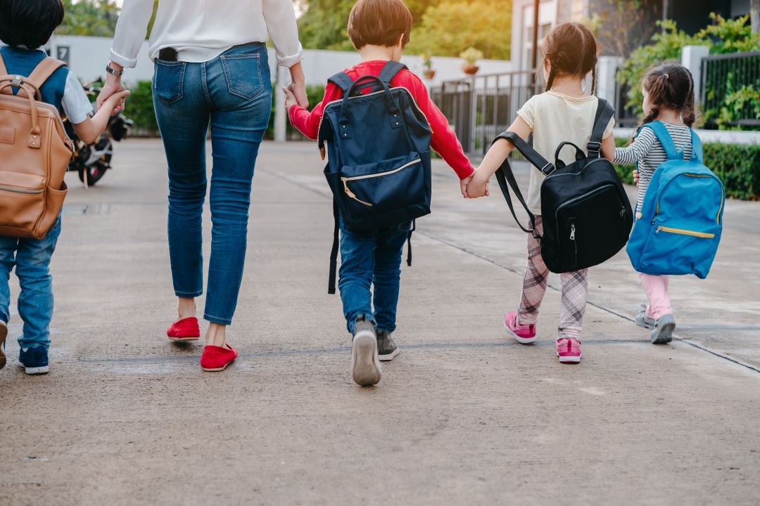 Madre e hijos tomados de la mano hacia la escuela de mañana.