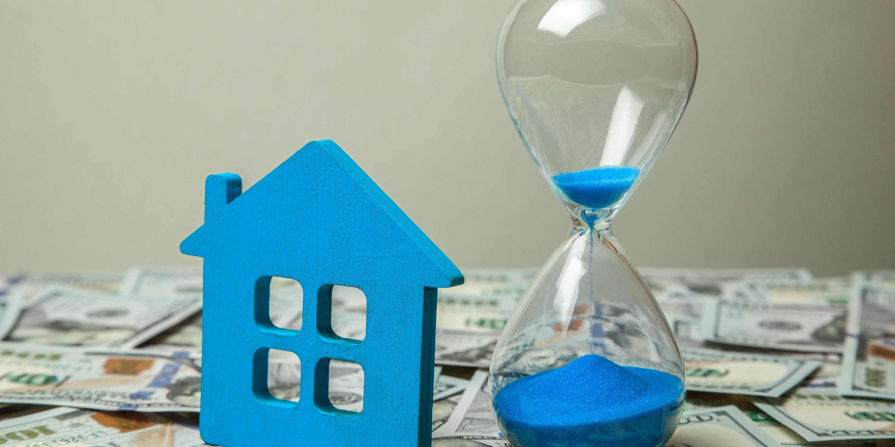Casas reposeísdas por el banco. Figura de casas al lado de un reloj de arena azules. Hay dinero debajo.