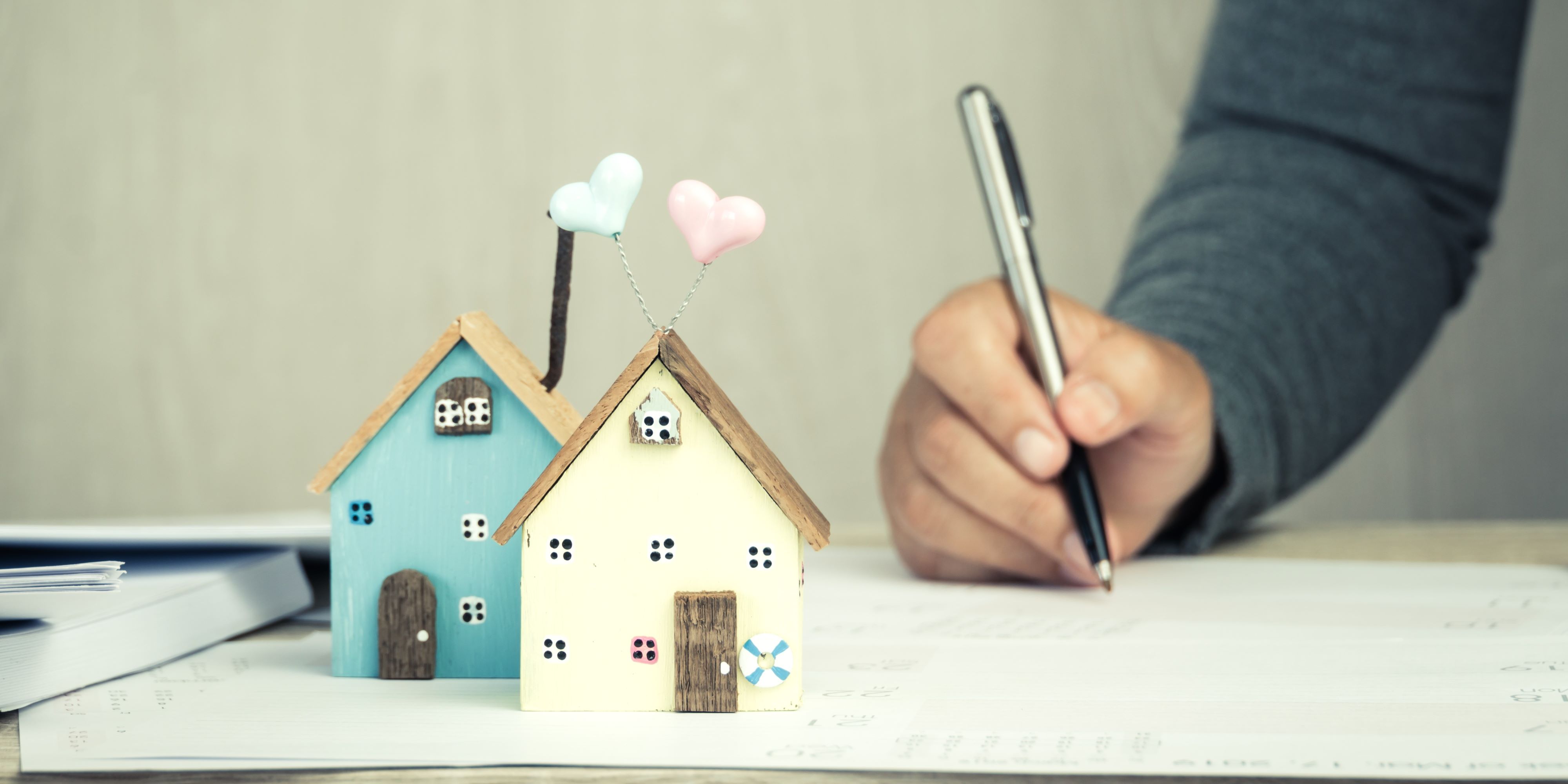 ¿Qué es un aval y cómo funciona? En un escritorio, hay un hombre con una pluma firmando un contrato. También hay dos casitas su escritorio.