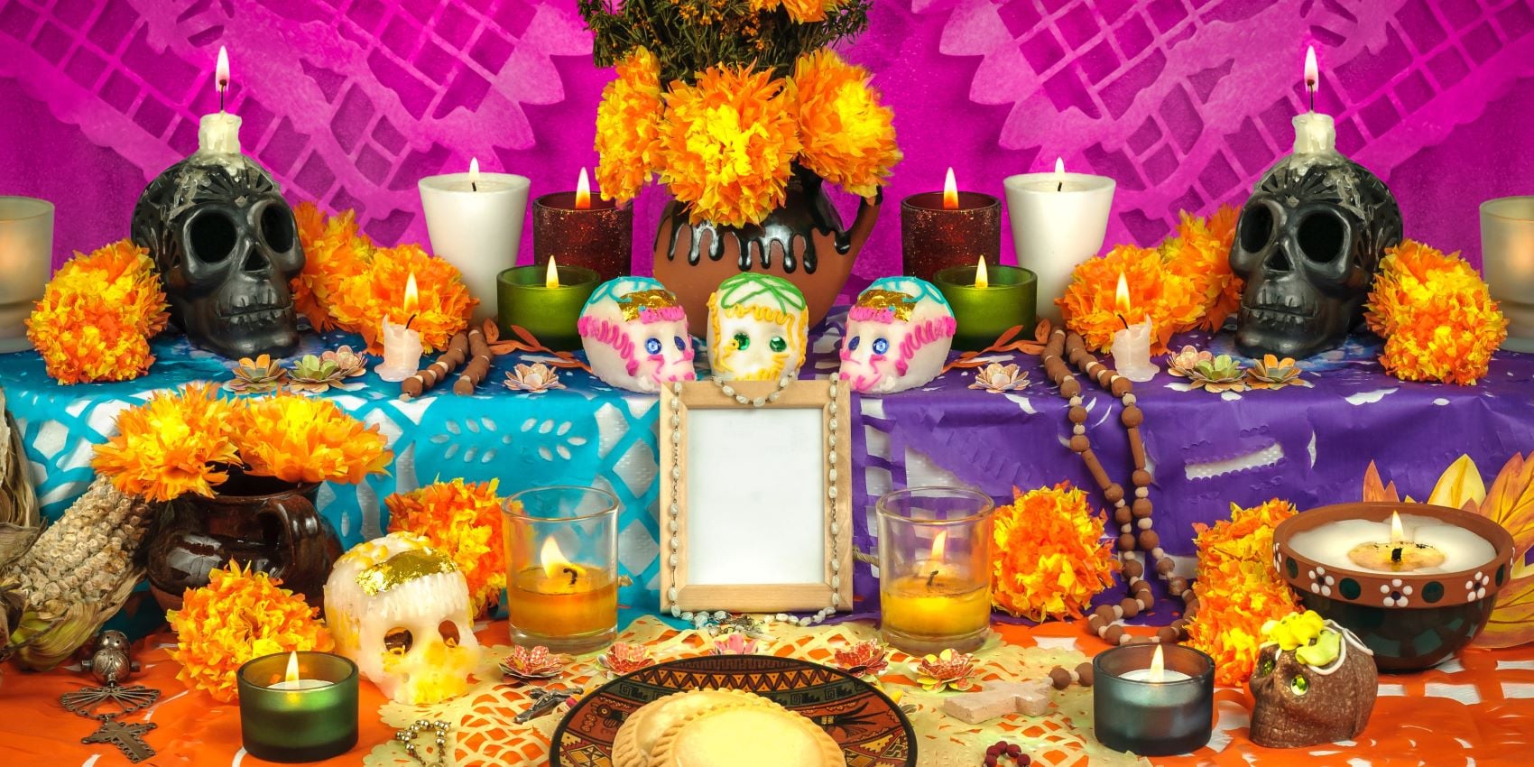 Ofrenda del día de muertos. Hay calaveritas de azúcar, velas, una fotografía en blanco, flor de cempasúchil, y más.