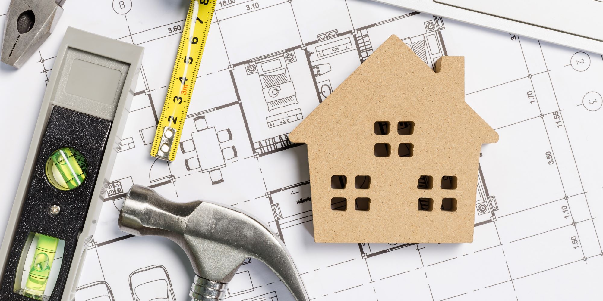 Planos, con una casa, martillo, regla y demás herramientas, para hacer mantenimiento de una casa. Está la figura de madera de una casita encima.