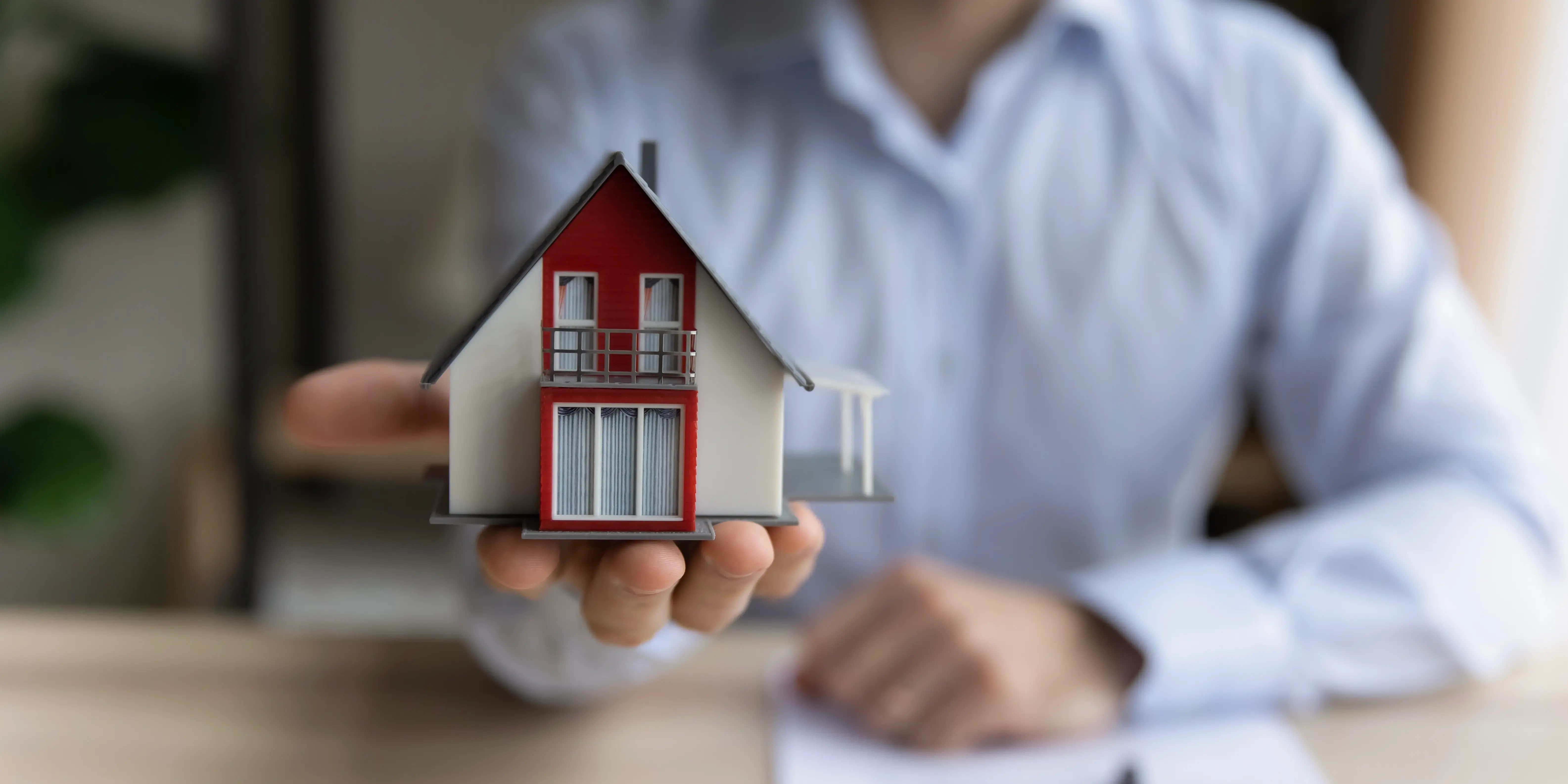 Asesor inmobiliario sosteniendo casa. Crédito hipotecario y autofinanciamiento