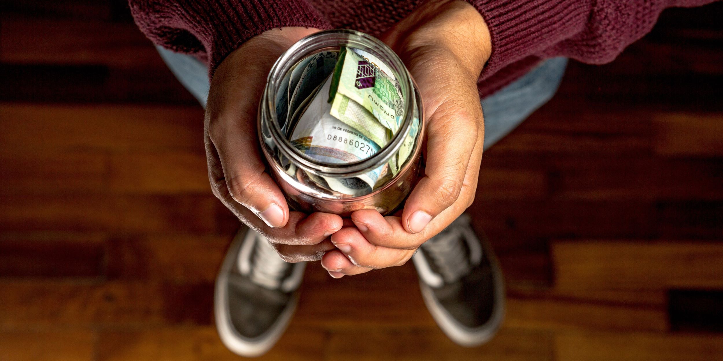 Hombre joven sostiene un frasco con dinero que representa su aguinaldo, y sus intenciones de ahorrarlo para aprovecharlo mejor.