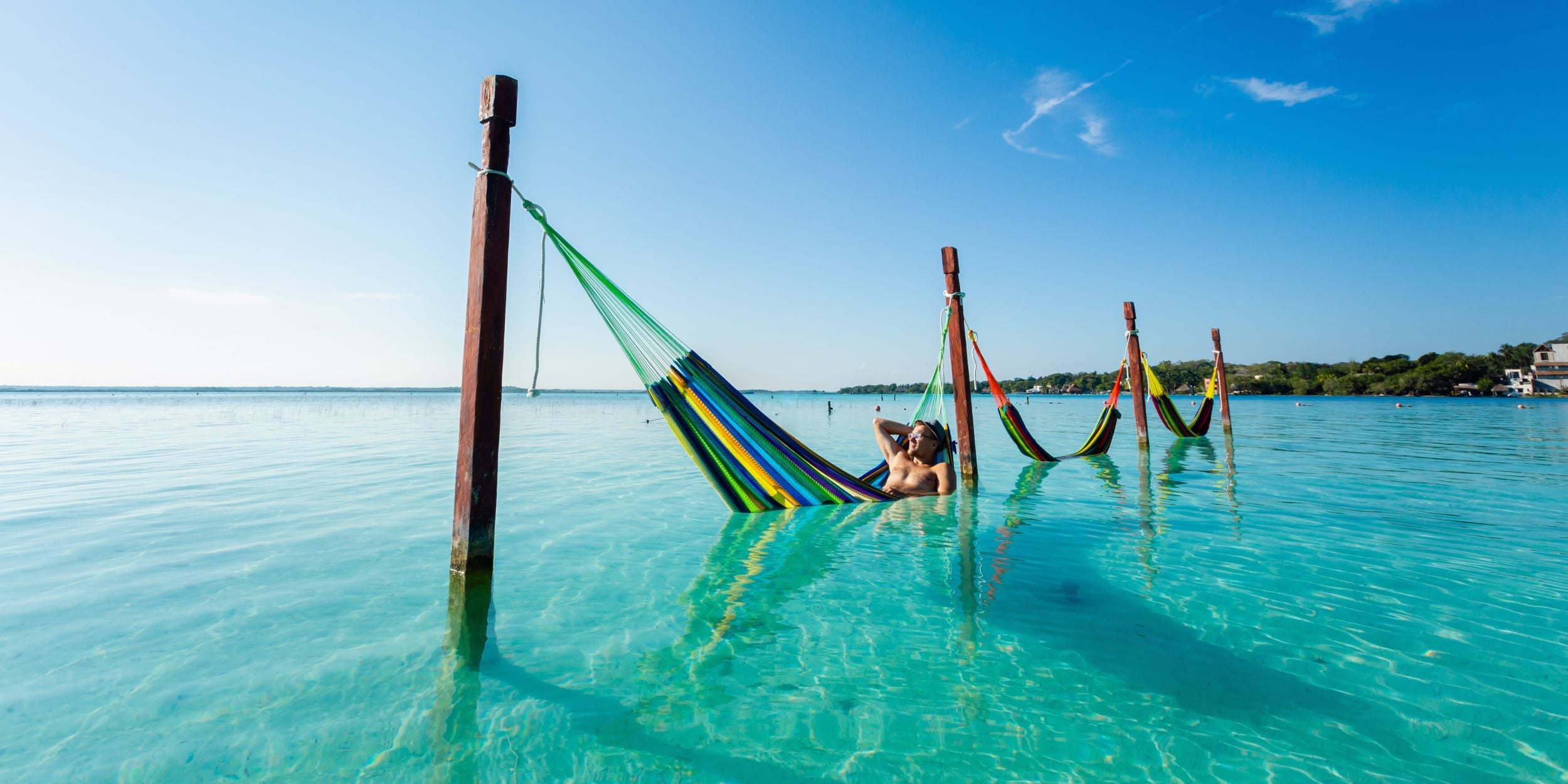 Persona descansando en una hamaca, en medio del mar. Está en Cancún, disfrutando del buen clima de la playa.