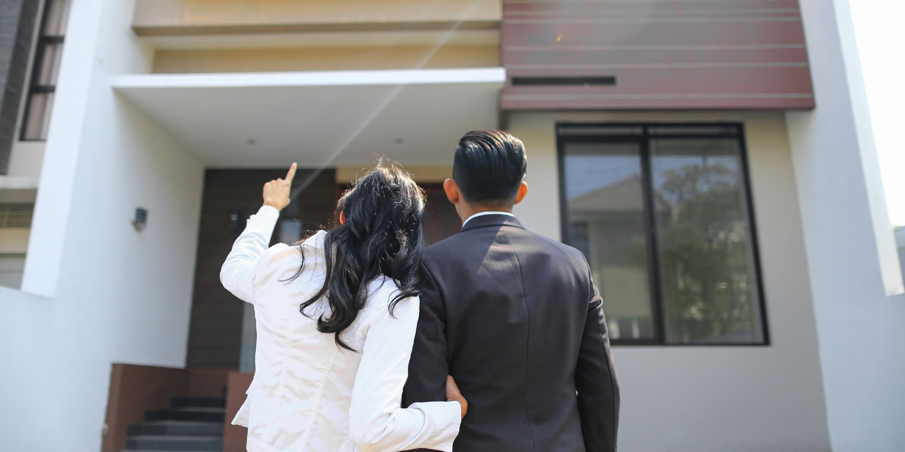 Pareja está buscando comprar casa. Están frente a la fachada de uan casa.