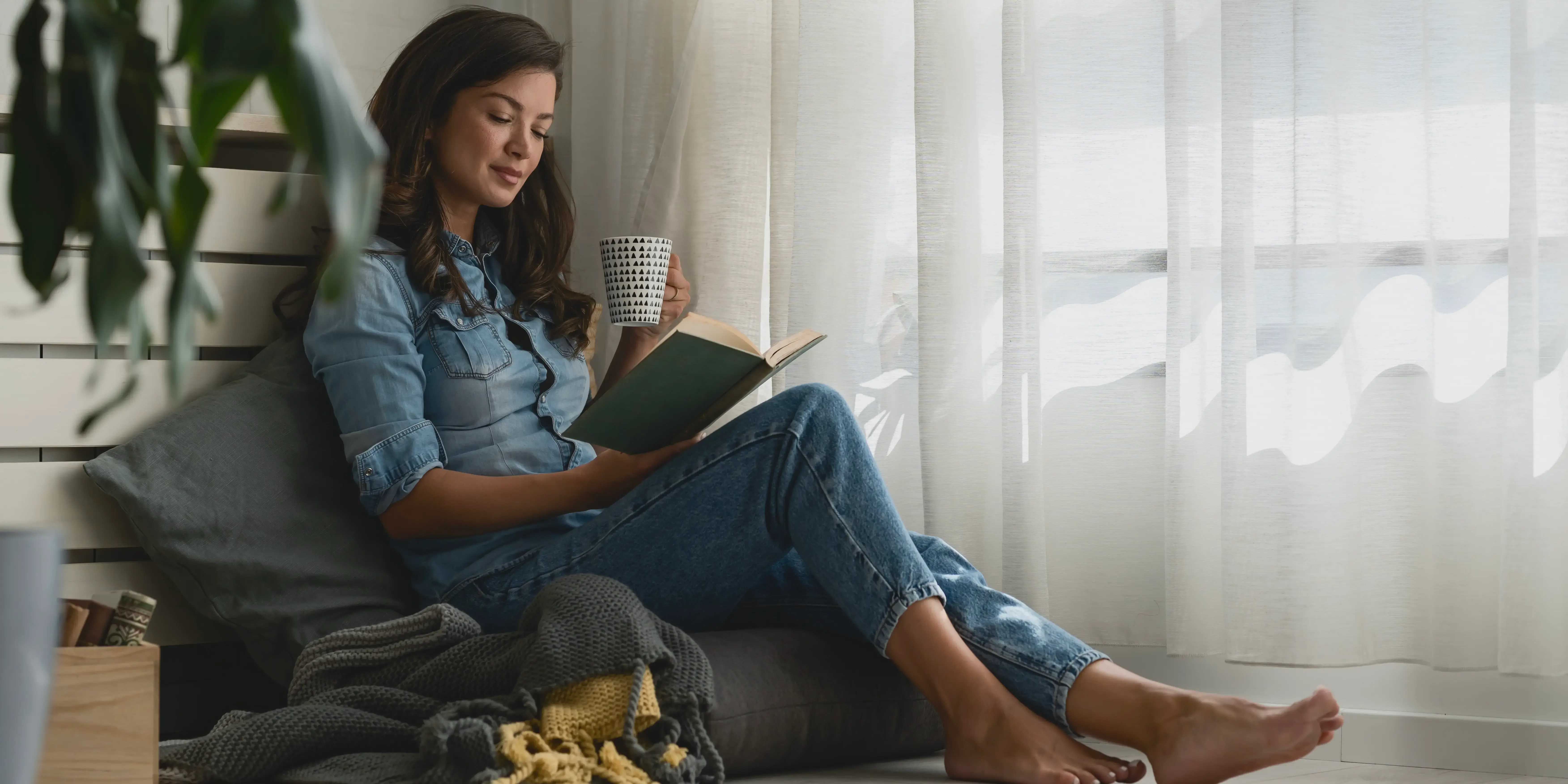 Mujer relajada leyendo un libro en un rincón de la casa. Bienestar emocional