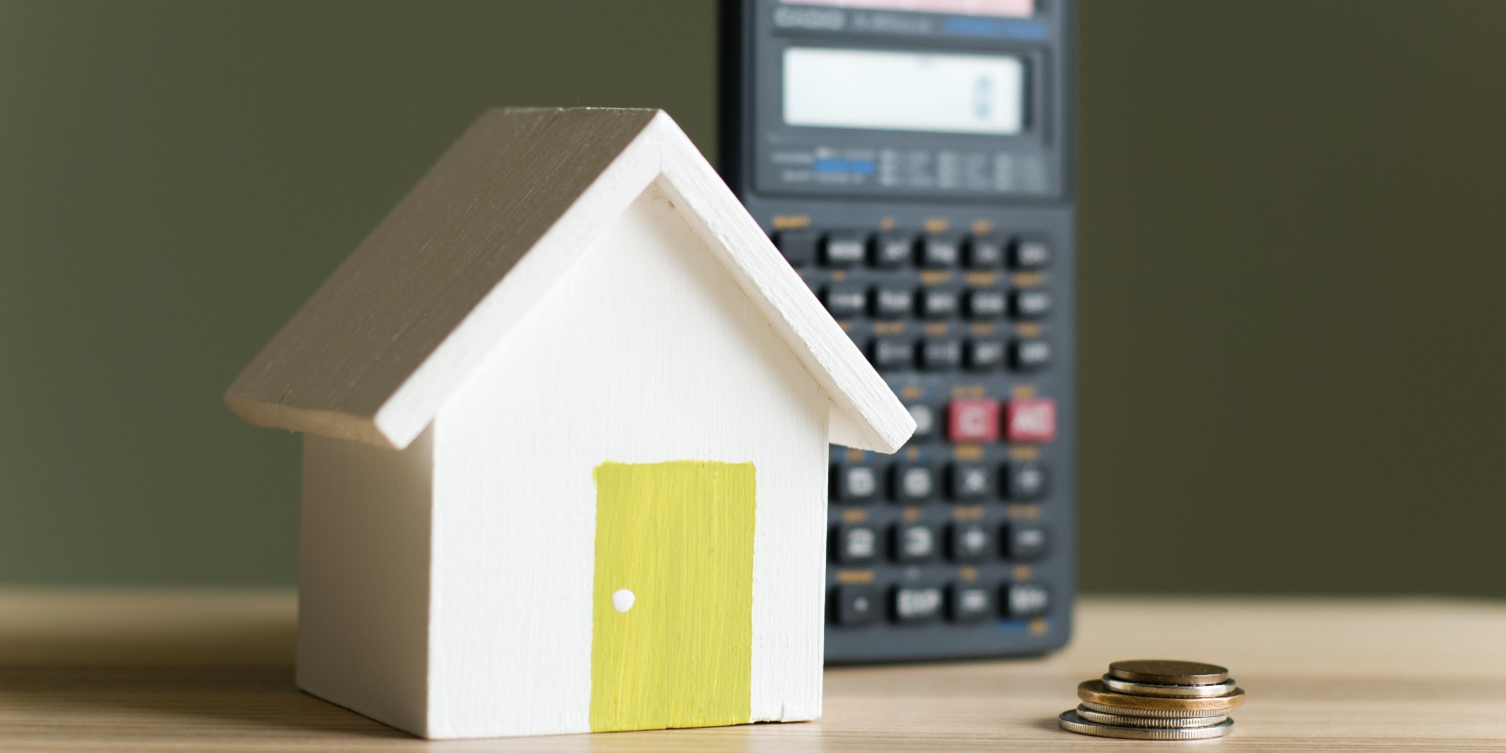 Ahorro para el enganche de una casa. Casita de madera junto a una calculadora y un montón de monedas.