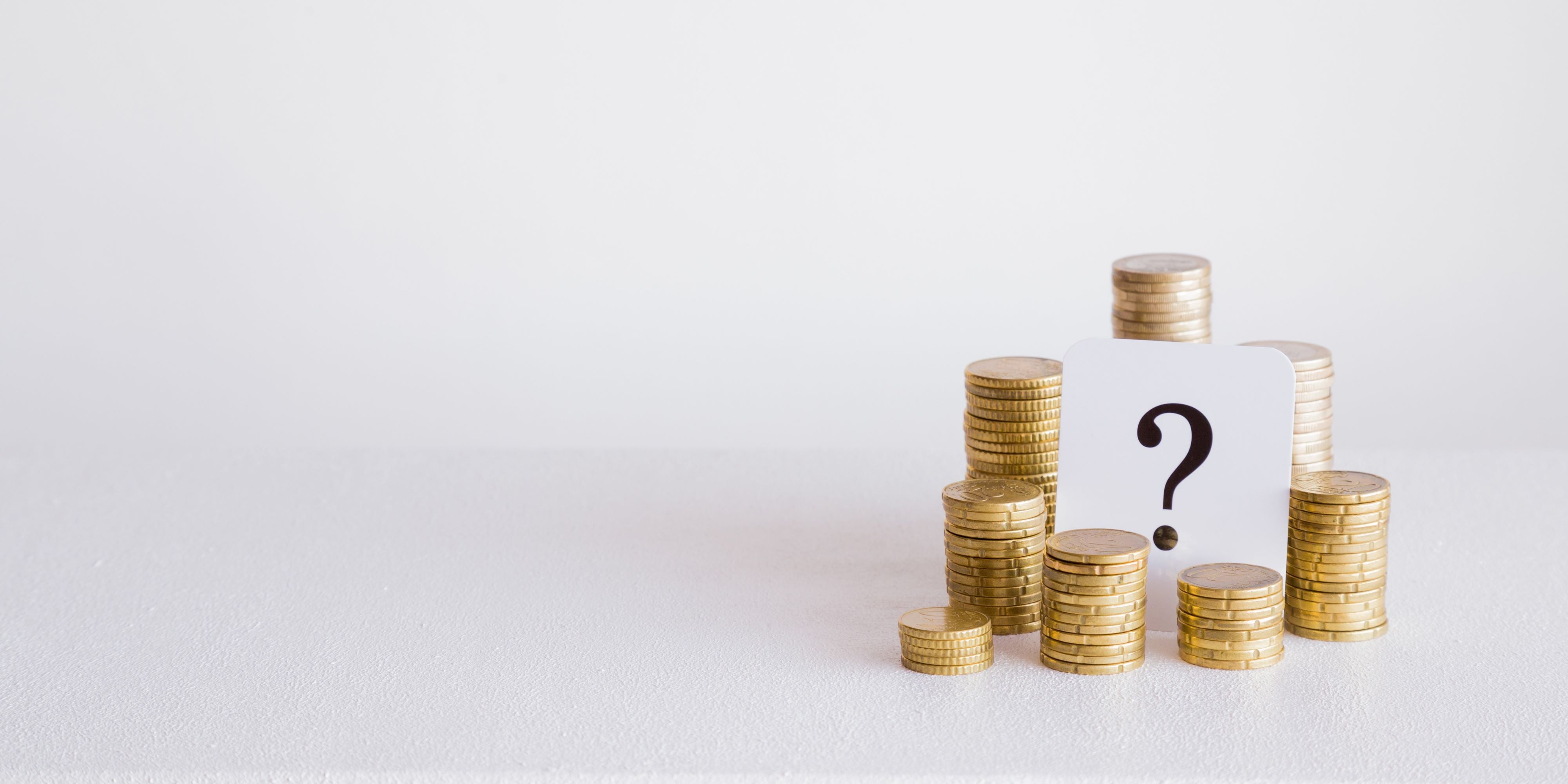 Mitos sobre la cuesta de enero. Un montón de monedas con un cartel cuyo contenido es un signo de interrogación, representa las dudas financieras.