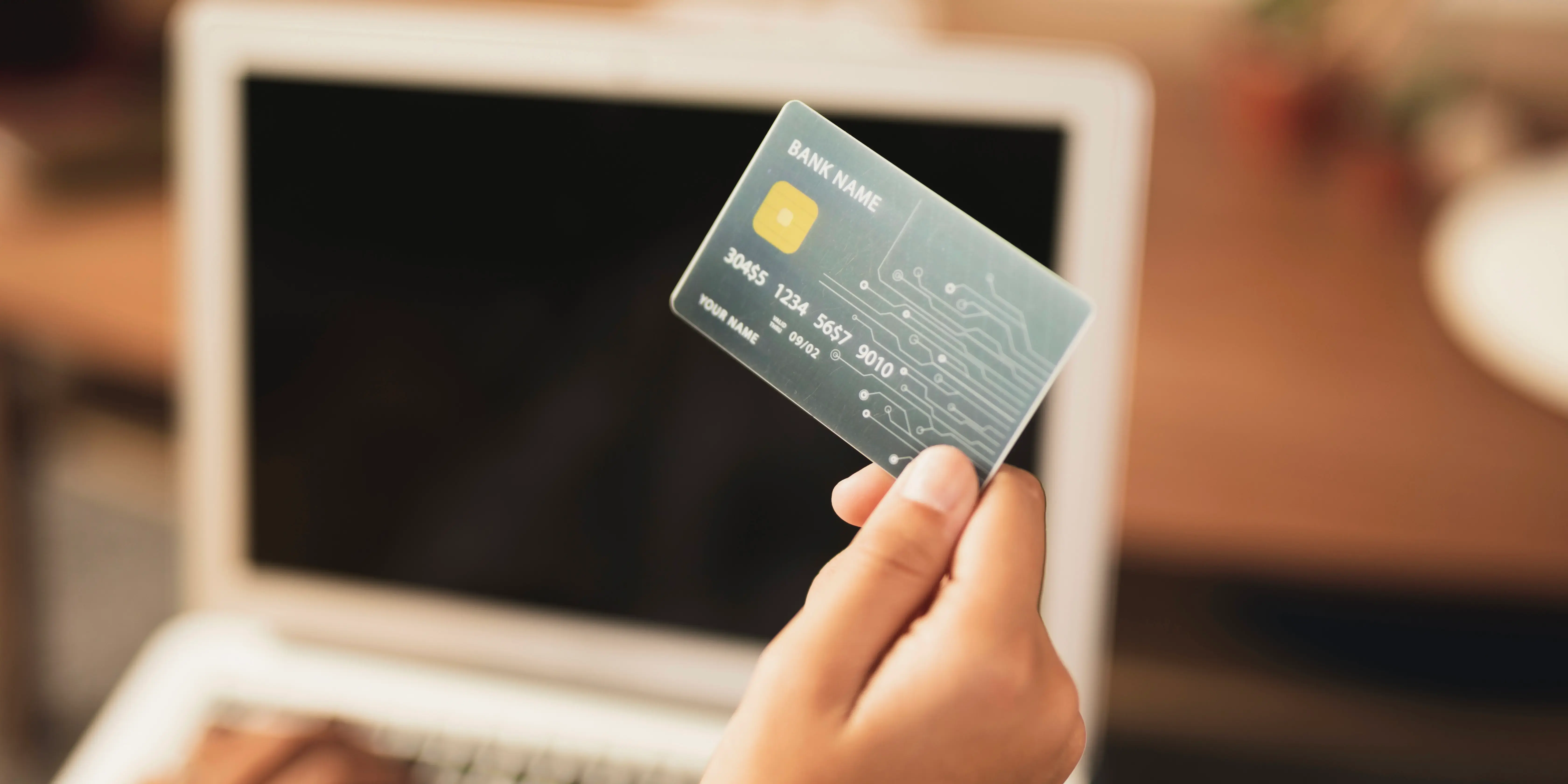 Persona en computadora sosteniendo tarjeta de crédito. Mejorar tu historial crediticio